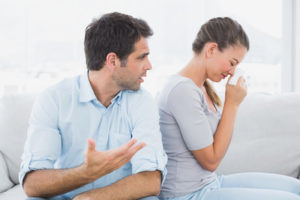 Man pleading with his crying partner on the couch at home in the living room